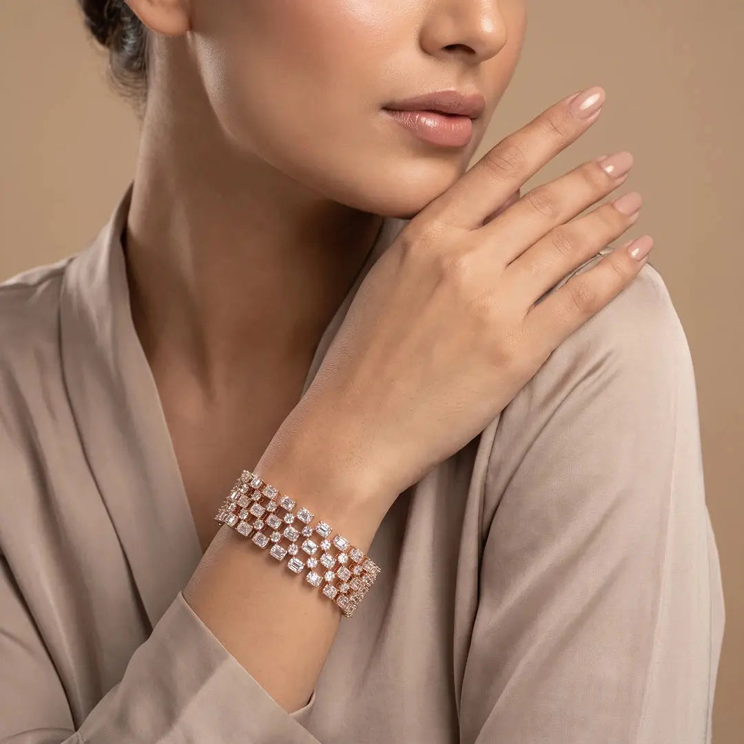 A close-up of a model wearing a wide rose gold cuff bracelet with sparkling clear diamonds, styled with a beige satin robe against a warm beige background.