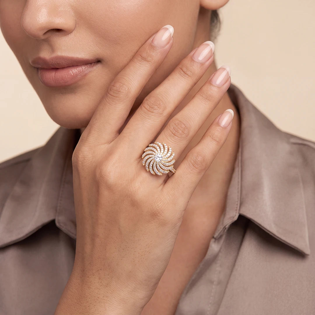 A close-up lifestyle shot of a model wearing a white gold spiral-patterned ring on her finger, with her hand resting near her face against a soft beige background.